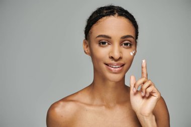 A beautiful young African American woman, topless, holds up a peace sign against a grey background. clipart