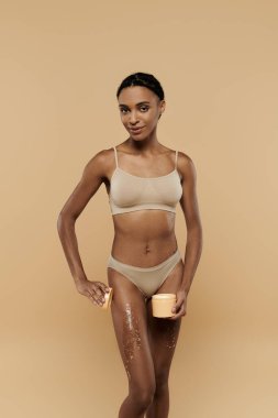 Bikinili, ince Afrikalı Amerikalı bir kadın bej bir arka planda bacaklarında şeker fırçasıyla poz veriyor..