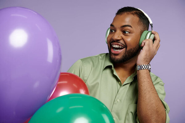 A cheerful young African American man in braces donning headphones and a green shirt, listening to music.
