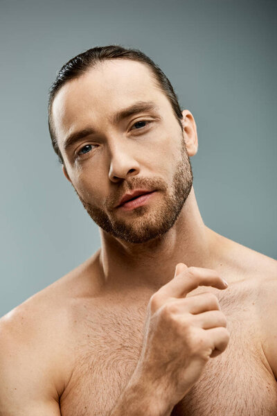 A shirtless man exudes masculinity with his rugged beard in a studio setting against a grey backdrop.