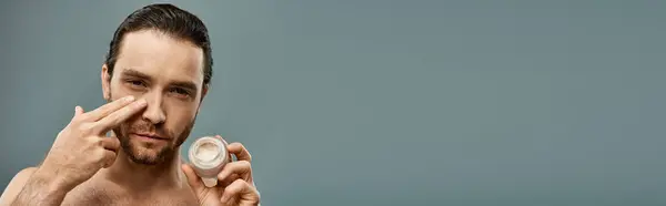 stock image Shirtless man with a beard holding a jar of cream against a grey background.