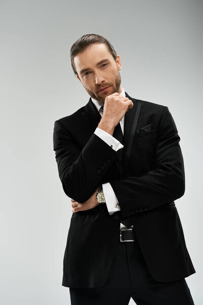 A bearded businessman in a stylish suit and tie strikes a confident pose against a grey studio background.