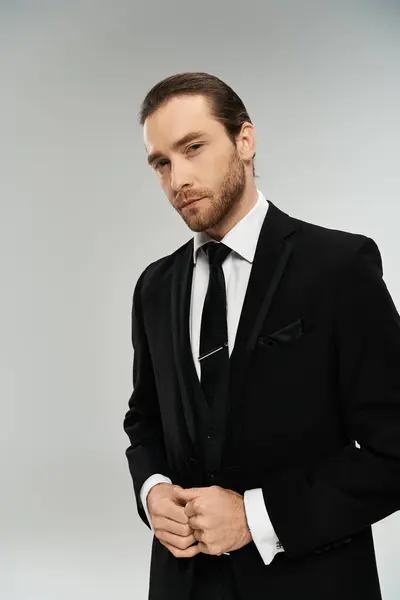 stock image A charismatic, bearded businessman in a sharp suit and tie strikes a confident pose on a grey studio background.