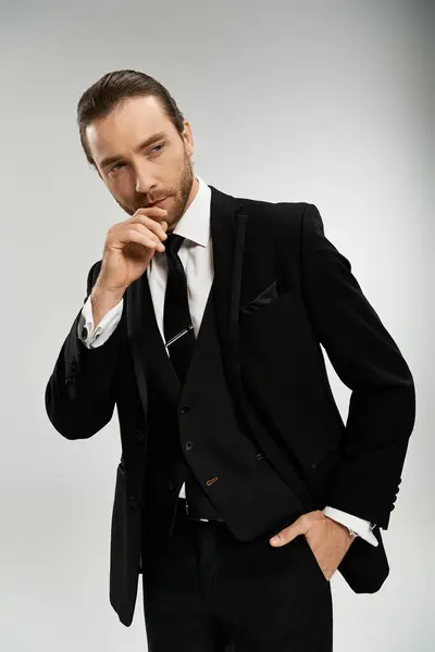 stock image A handsome and bearded businessman confidently poses for a portrait in a stylish tuxedo against a neutral grey background.