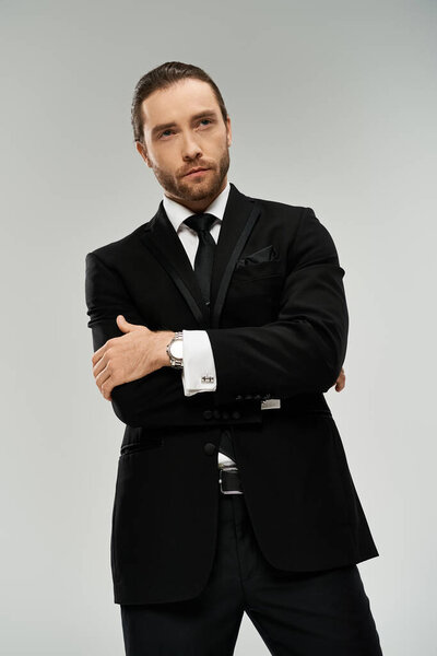 Bearded businessman in a suit and tie confidently stands with his arms crossed against a grey studio background.
