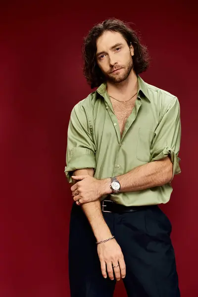 stock image A stylish man with glasses strikes a pose in a green silk shirt against a striking red background.