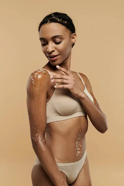 stock image Slim African American woman covered in scrub, posing confidently in a bikini on a beige background.