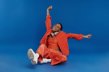 Parlak turuncu elbiseli bir kadın yerde dinleniyor. Huzurlu bir yansıma anında..