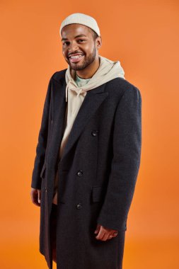 Ceketli ve şapkalı Afro-Amerikalı adam turuncu arka planda duruyor..