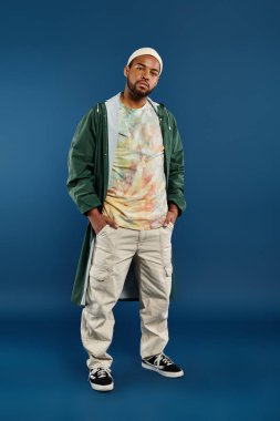 Zarif Afro-Amerikalı adam canlı mavi bir arkaplanın önünde kendinden emin bir şekilde duruyor..