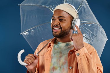 Şık bir Afrikalı Amerikalı şemsiye tutuyor ve kulaklık takıyor..