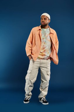 Beyaz şapkalı ve turuncu ceketli şık bir adam canlı arkaplanda poz veriyor..