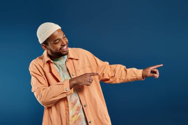 African American man in orange shirt energetically points towards something off-frame. clipart