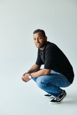 An African American man in a black shirt and jeans kneels down on a vibrant backdrop. clipart