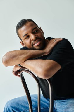 Kollarını kavuşturup sandalyede oturan şık Afro-Amerikan adam..