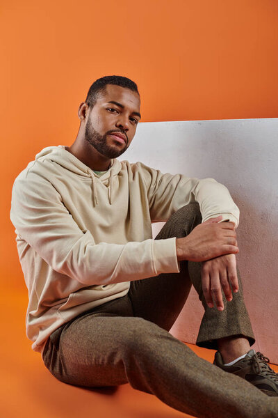 Стильный афроамериканец сидит изящно на ярком фоне.