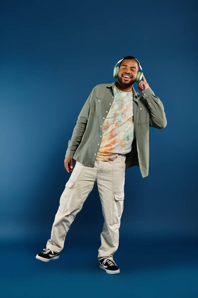 A stylish African American man stands in front of a blue background while wearing headphones.
