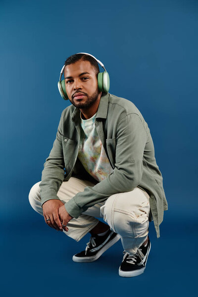 Стильный афроамериканец сидит на земле в наушниках.