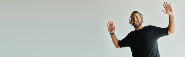 Black-shirted man energetically raises his hands, standing confidently.