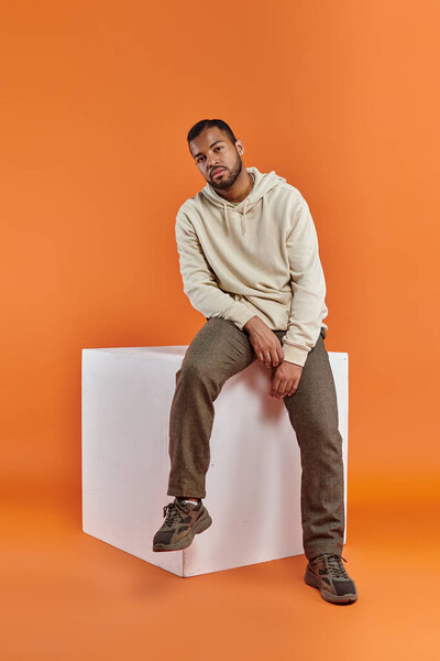 A stylish African American man seated atop a white cube.
