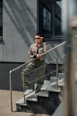 Modern binanın yanındaki merdivenlerde şık giyinmiş genç bir kadın duruyor..