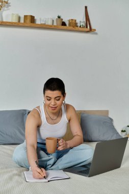 A young woman with short hair in casual wear sits on a bed, engrossed in her laptop. clipart