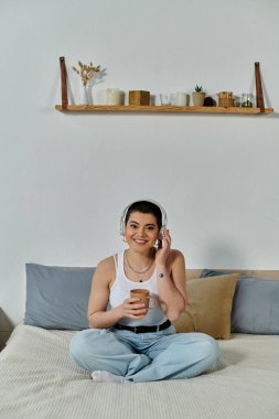 Kısa saçlı genç bir kadın yatakta oturmuş kulaklıkla müzik dinlemekle meşgul..