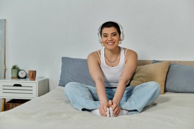 Kısa saçlı bir kadın, yatakta kulaklık takarak müzik dinlemekten hoşlanır..