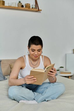 Kısa saçlı genç bir kadın bir yatakta oturuyor, kendini evinde günlük kıyafetleriyle kitap okumaya kaptırmış..