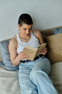 Bir kadın rahat bir ev ortamında bir yatakta otururken kendini bir kitaba daldırıyor..