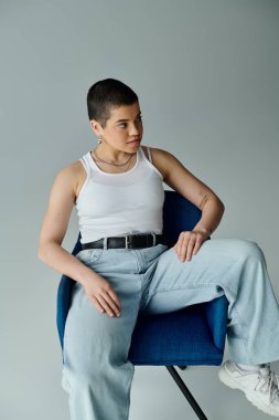 Kısa saçlı genç bir kadın zarif bir şekilde sandalyede oturuyor, sakinlik ve rahatlama hissi yayıyor..