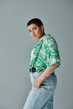 Kısa saçlı genç bir kadın şık yeşil bir gömlek ve kot pantolon giyiyor..