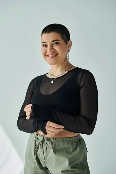 stock image A young woman with short hair strikes a pose in trendy casual clothing against a grey background.