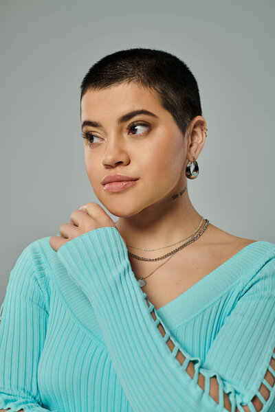 Молодая женщина с короткими волосами позирует в стильной повседневной одежде на сером фоне.