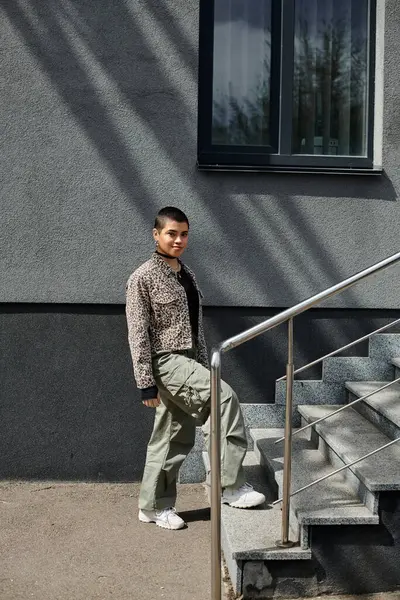 stock image A young woman in stylish attire and leopard print jacket walks up the steps of a modern building.