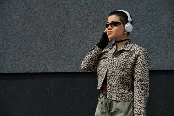 stock image A stylish woman in leopard print jacket walks down a city street while listening to music on headphones.