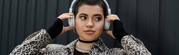 stock image A stylish young woman with short hair wearing headphones listens to music near a modern building.