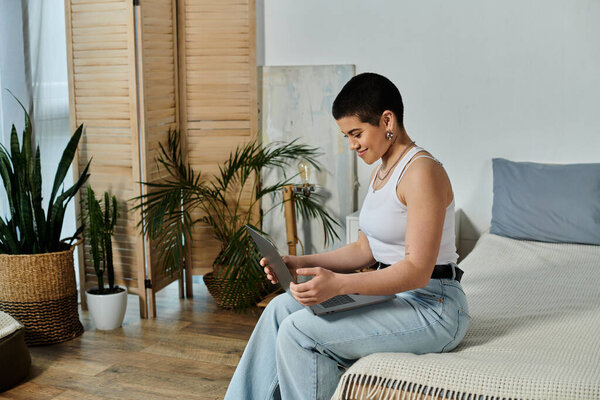 Молодая женщина с короткими волосами, лежащая на кровати, зацикленная на ноутбуке в повседневной одежде дома.