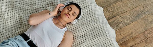 A man in casual wear lies on a bed, engrossed in music