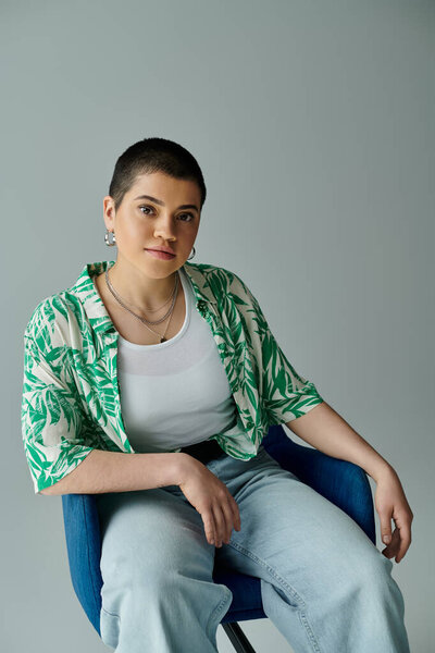 A young woman with short hair is peacefully seated in a blue chair, wearing a green shirt.
