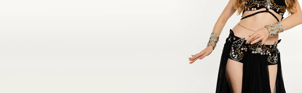 A captivating woman dressed in a black and gold costume gracefully performs a mesmerizing belly dance.