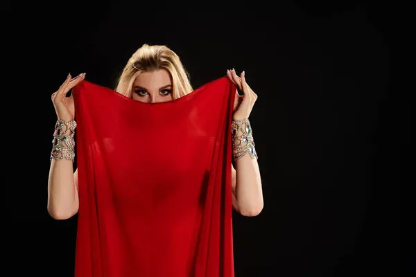 stock image A captivating woman in a red dress gracefully holds a scarlet cloth while performing a mesmerizing dance.