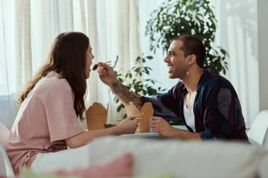 Gey bir çift gündelik giysiler içinde keyifli bir anın tadını çıkarıyor, masada oturuyor ve yemeklerini paylaşıyorlar.