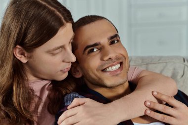 a gay couple, in casual clothes happily hugging on a cozy couch at home. clipart