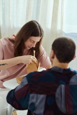 Gey bir çift gündelik giysiler içinde bir masada birlikte yemek yiyor, samimi anlar ve evde kaliteli zaman geçiriyor..