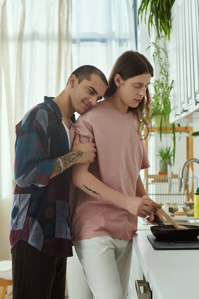 A gay couple in casual clothes stands side by side, engaged in conversation and food preparation in a warm, cozy kitchen.