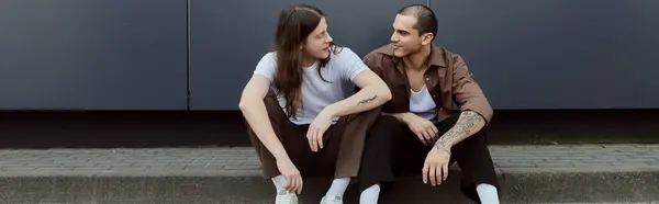 stock image a gay couple, sitting on asphalt in casual clothes, enjoying a peaceful moment together.