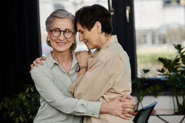 İki kadın pencerenin önünde nazikçe sarılıyor..