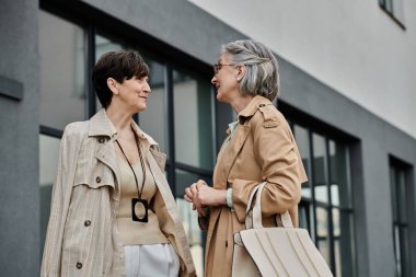 Modern bir binanın dışında sohbet eden iki zarif kadın..