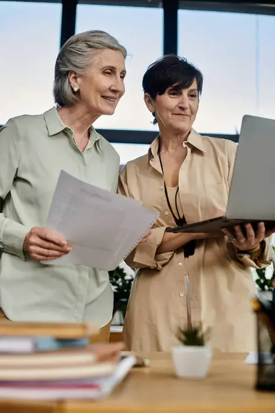 stock image Two women collaborate on a laptop in an office setting.